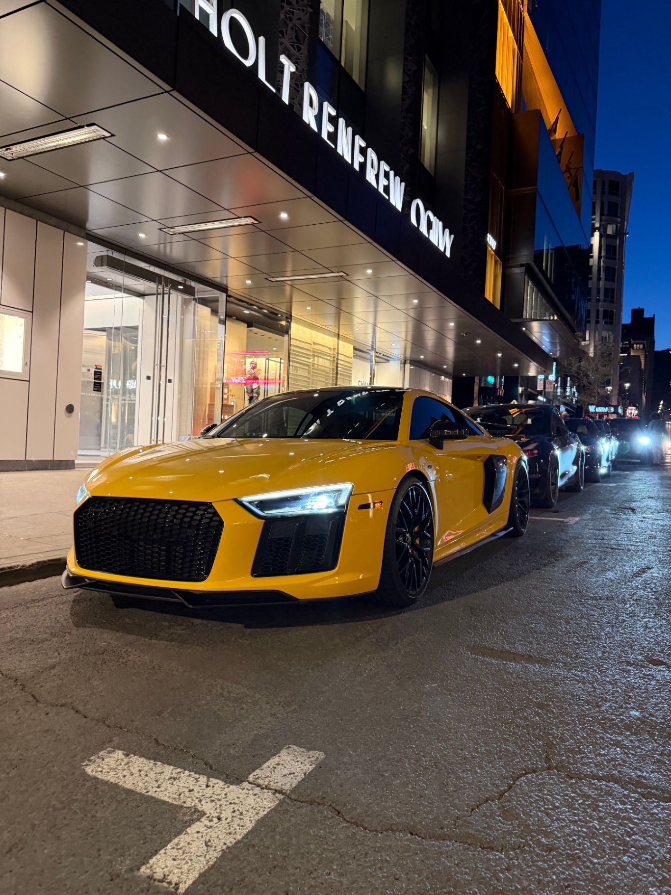 Audi R8 jaune la nuit devant les vitrines Holt Renfrew